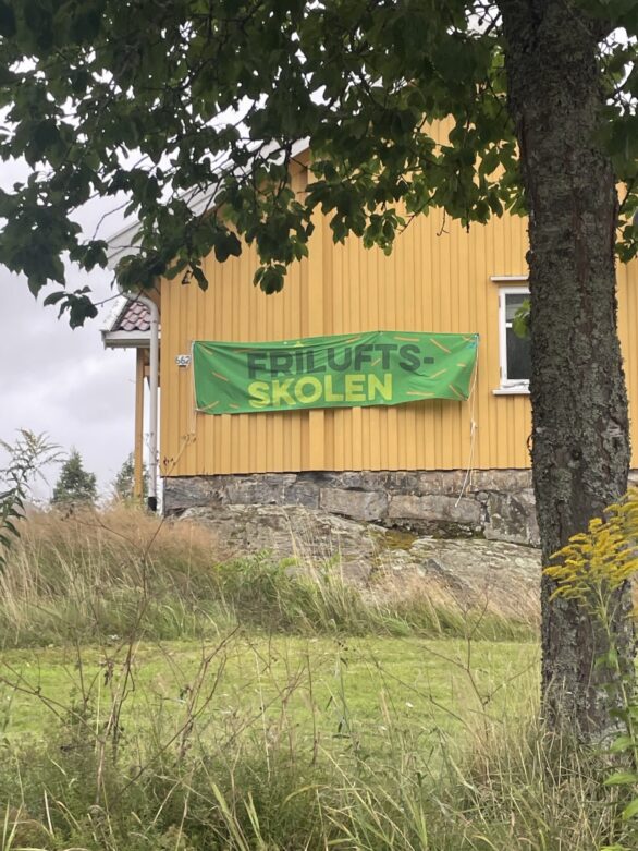 En gul husvegg med et banner det står Friluftsskolen på"