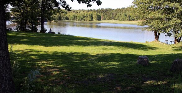Bilde av en stor plen med trær på hver side og vannet nedenfor.  Bakenfor vannet, på andre siden vises en åker og masse trær. Viser Rødsund badeplass.